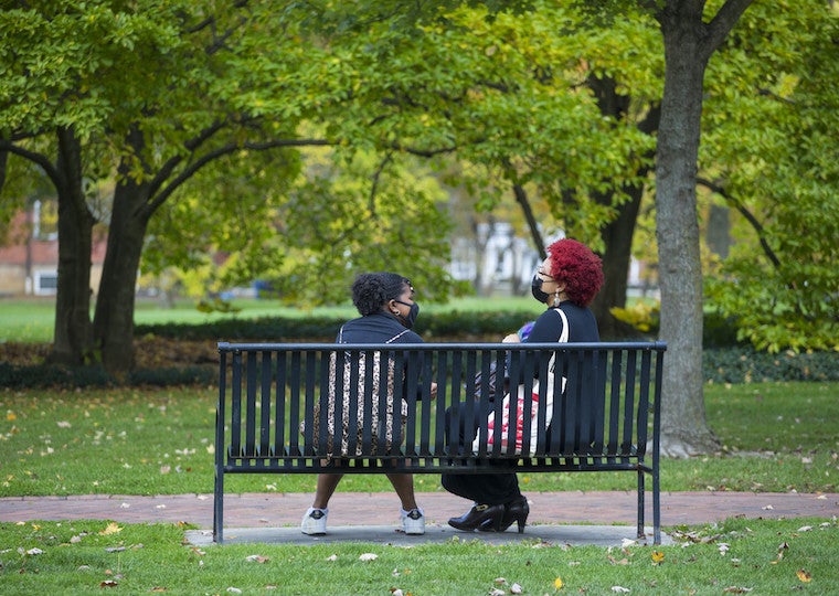 Two students sit on a bench in the park.