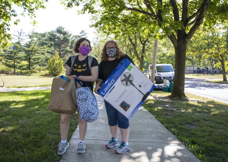 A parent and student wearing face masks hold boxes.