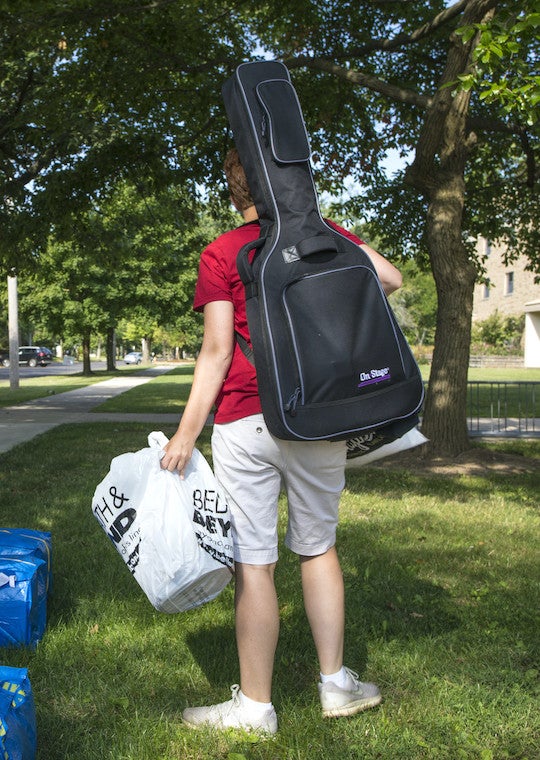 A student with a large guitar case on their back.