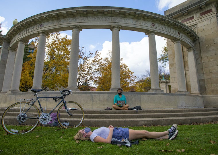 A student lays on the ground in front of large columns. 