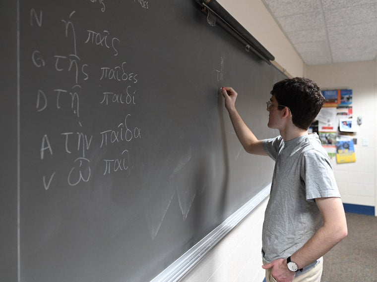A boy writes Greek letters on a blackboard.