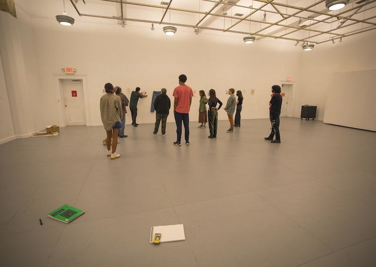 Students stand in a large empty room and look at artwork on a wall.