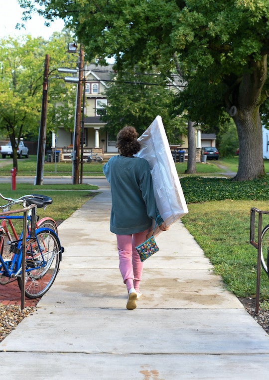 A girl walking with a large painting.