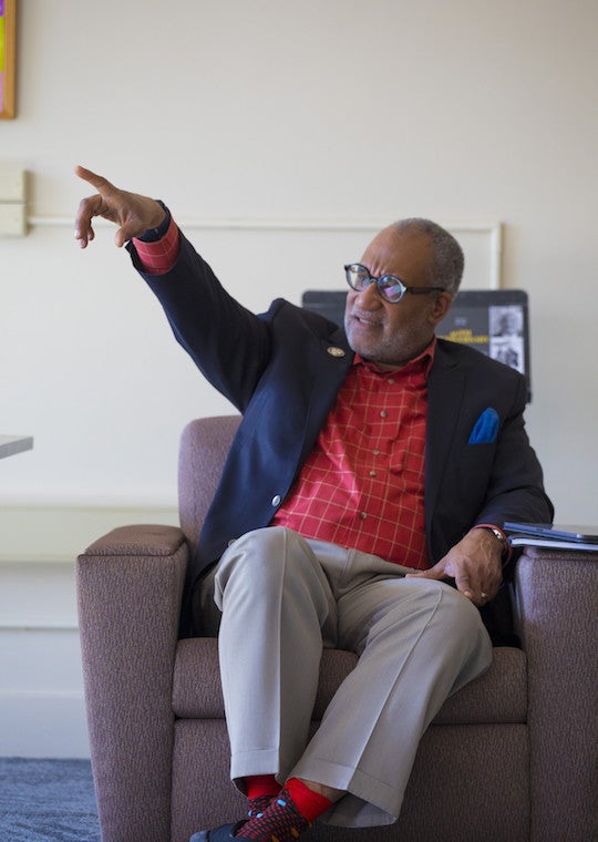 A man sits in a chair and points.