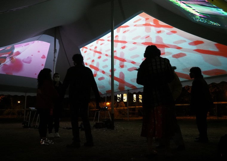 Images are projected on the inside roof of a tent with people walking inside. 