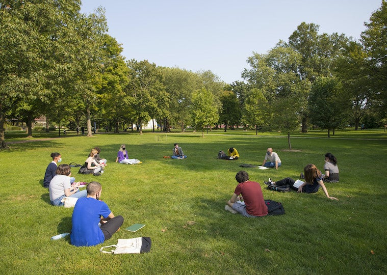 A large class sits in a round circle in the park.