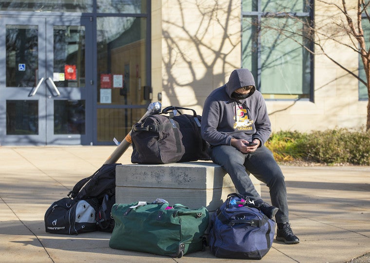 A student is surrounded by luggage while sitting in front of a building 