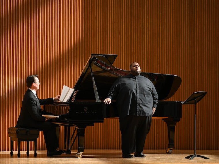 A man sings on stage with a man playing piano near him.