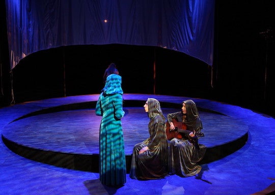 Three performers in shrouds act on a round stage floor.