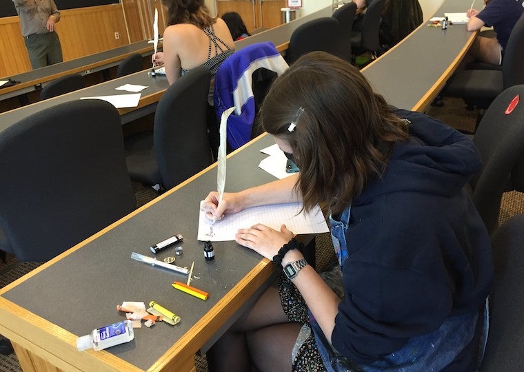 A girl writes with a quill pen.