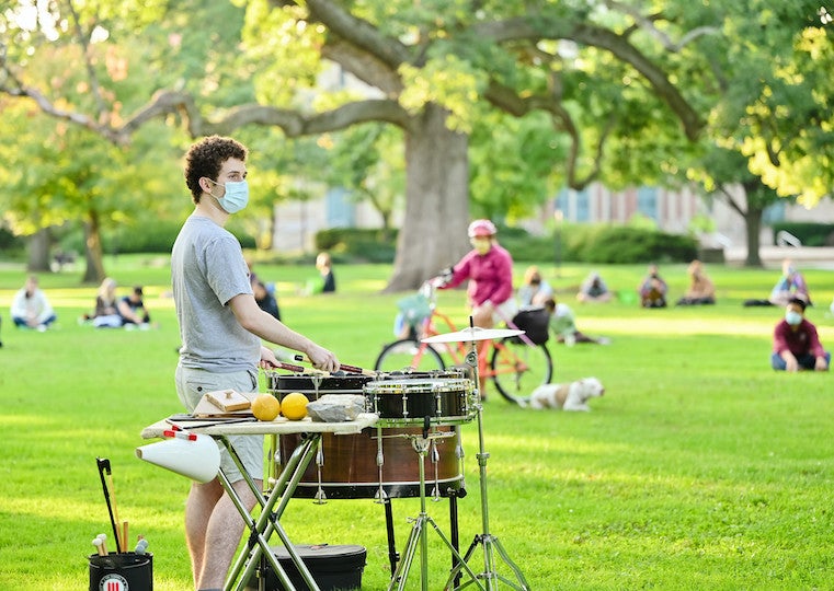 A student plays the drums in a park.
