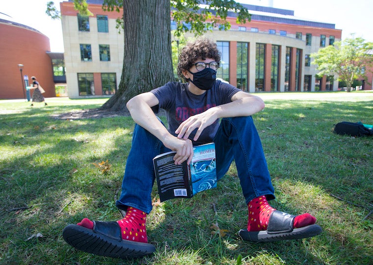 A student sits in the grass while holding a book
