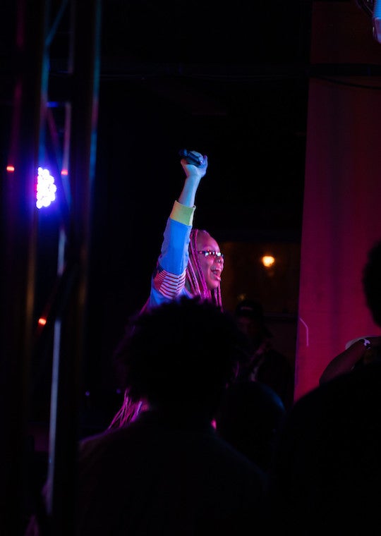 A female performer holds her hand and microphone in the air.