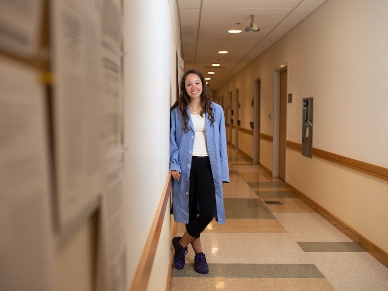 A girl wearing in long science coat stands in a long science center hallway.
