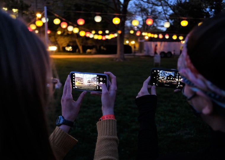 Two people take cell phone pictures of lanterns.