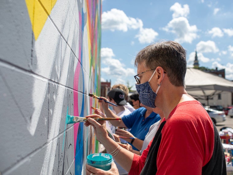 A woman paints a mural on a wall.