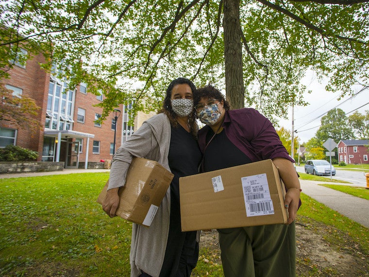 A mom and daughter stand close together while holding boxes.