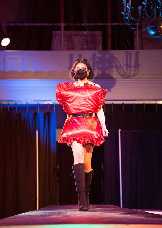 A girl with a pillow strapped to her front walks down a runway.