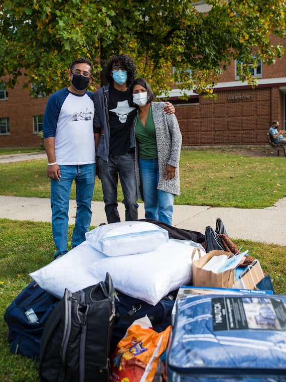 A family of three pose for a photo next to a pile of clothes on the ground.