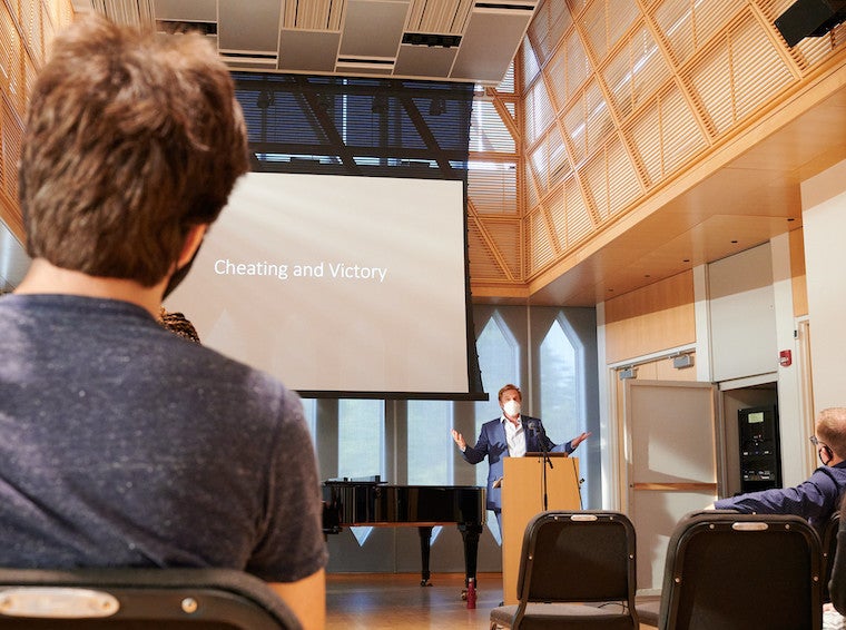 A male student looks at a large projector and man at a podium.