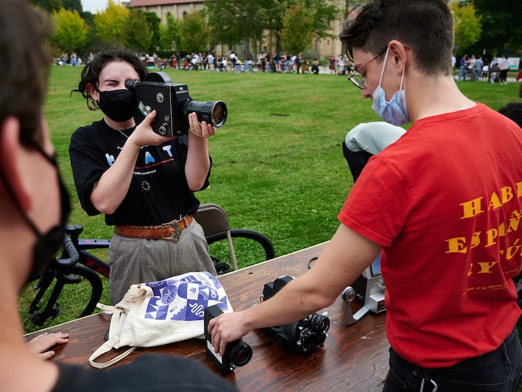 A college student holds a camera in front of another student.