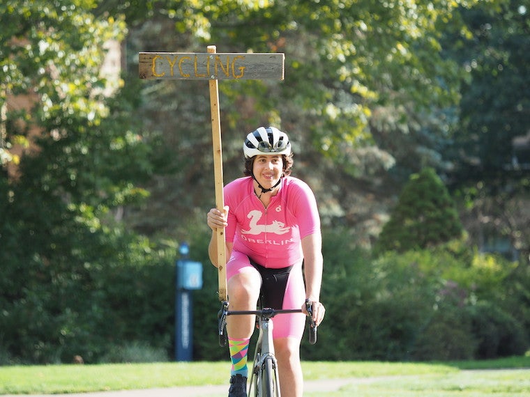 A girl holds a cycling club sign while riding a bike.