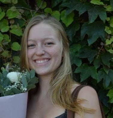 A portrait of a girl standing in front of a shrub,