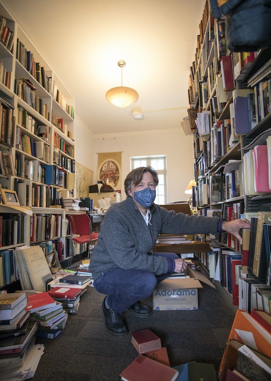 A man reaches for a book from an overcrowded bookcase.
