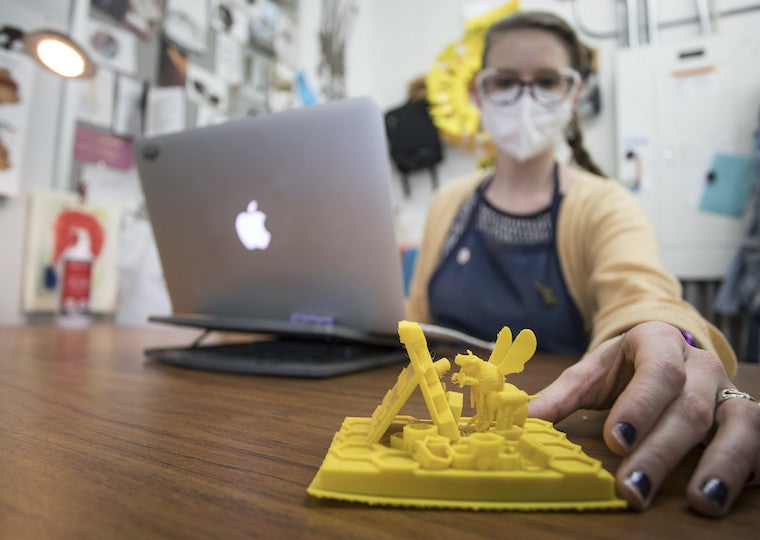 A woman places a 3D model of a bee and honeycomb on her desk.