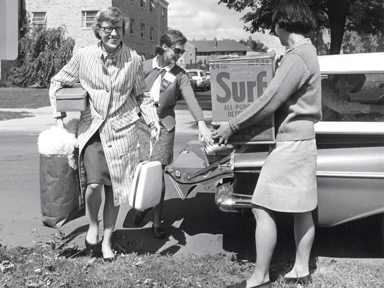 A woman helps two girls unload boxes from a station wagon.