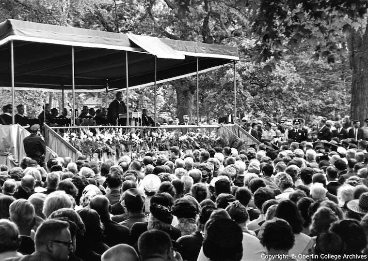 A large crowd looks at a man on a stage giving a speech.