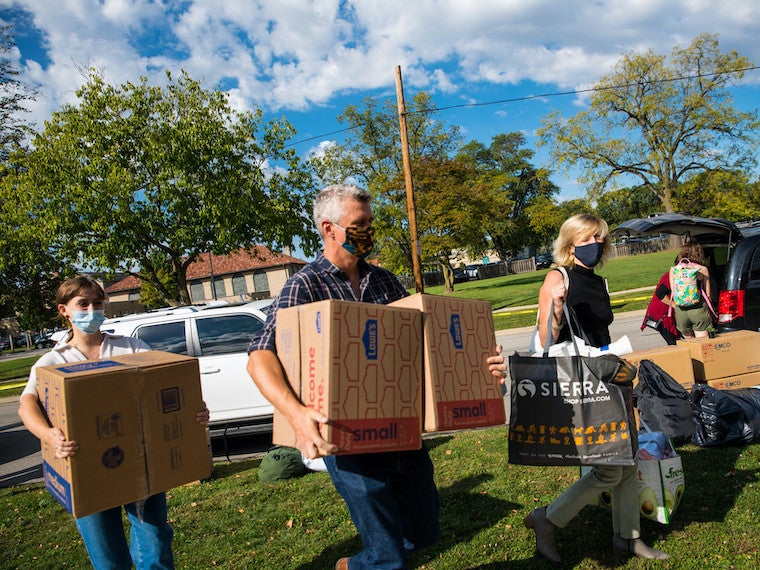 Four people carry boxes across a lawn.