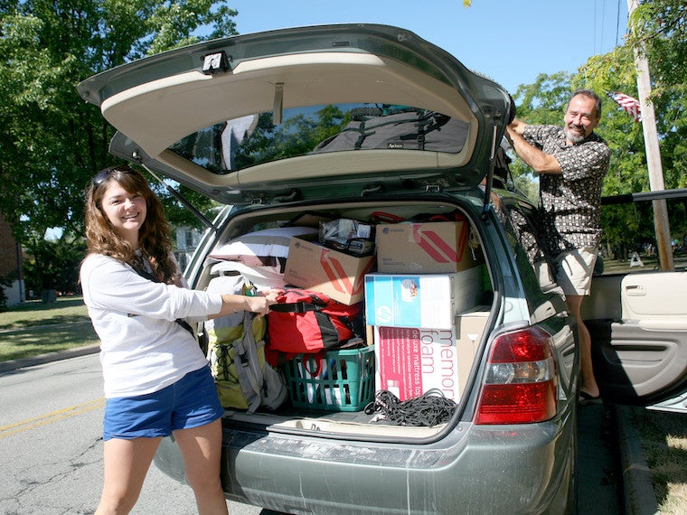 A girl and father unload a packed car.