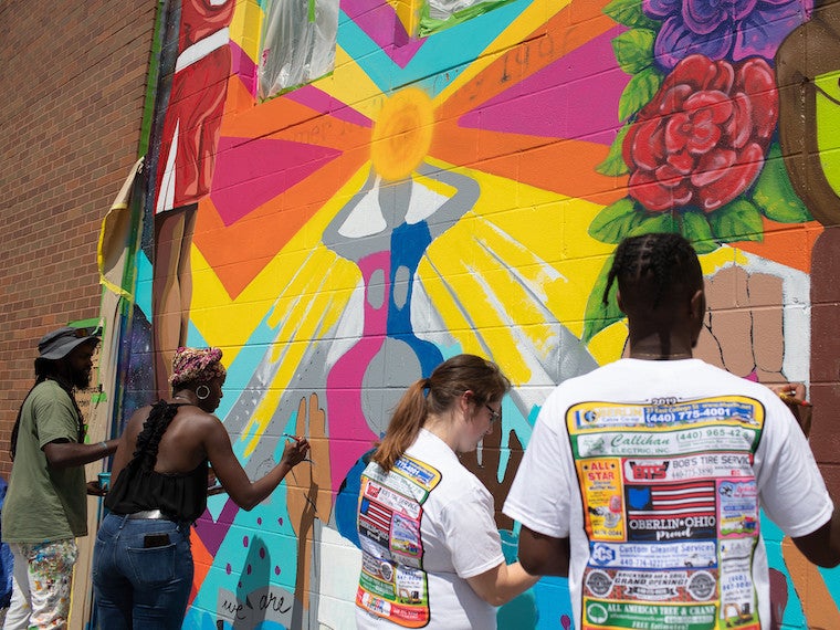 Three artist paint a mural on a wall.