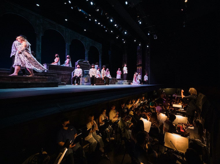 An orchestra plays in a pit while an opera performs on stage.