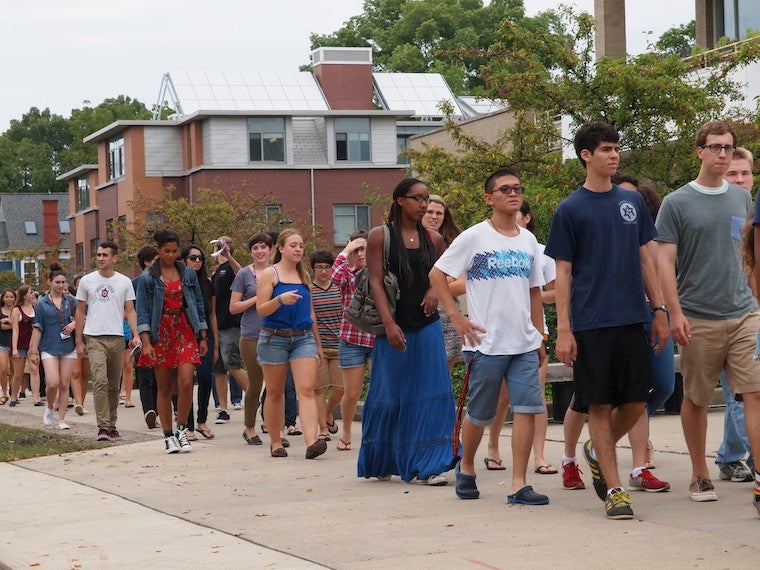 A large group of students walk down a sidewalk.