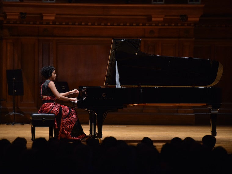 A girl plays a grand piano in front of an audience.