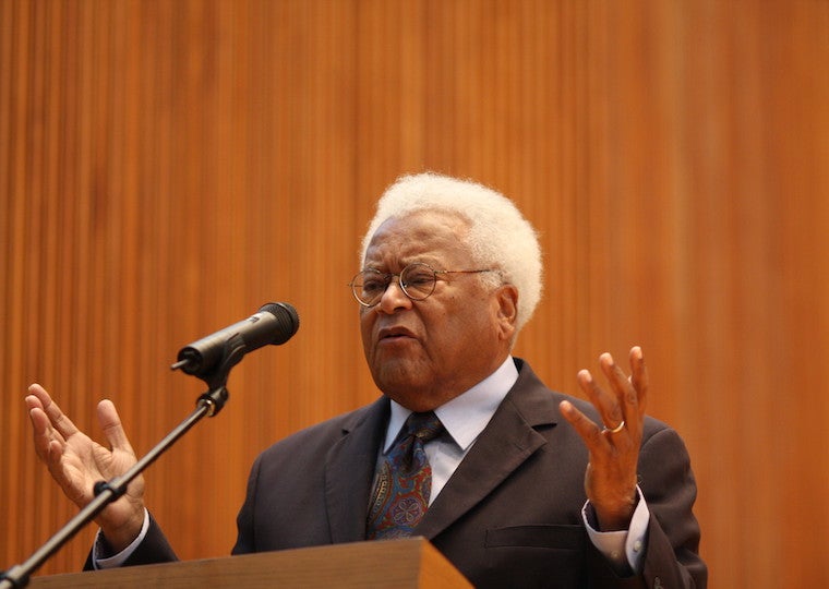 An elderly man gives a speech in front of a podium.