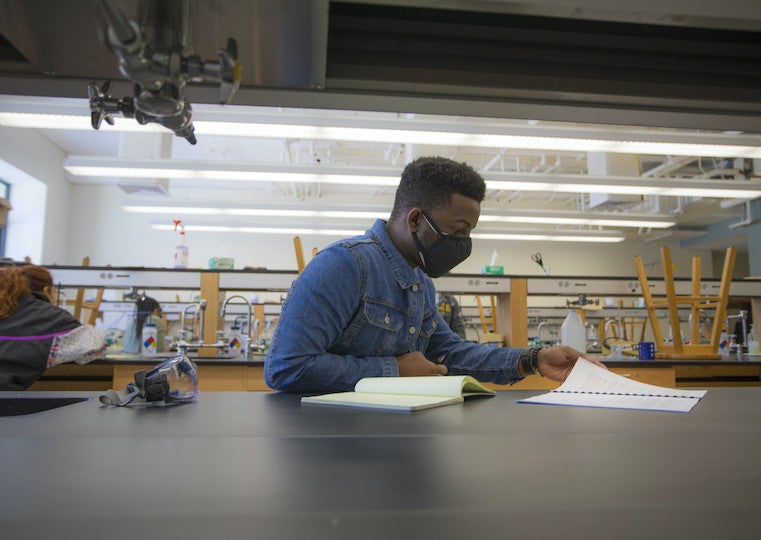 A male student turns pages in a binder at a lab table.