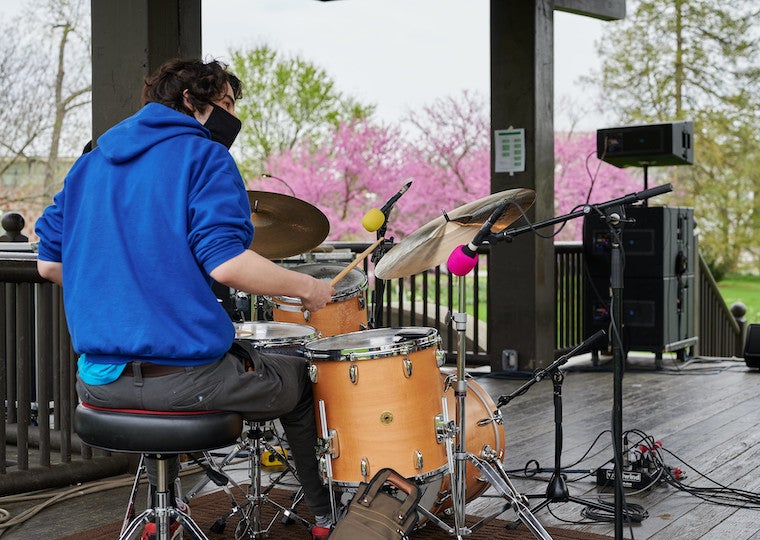 A male playing drums on a stage outside.