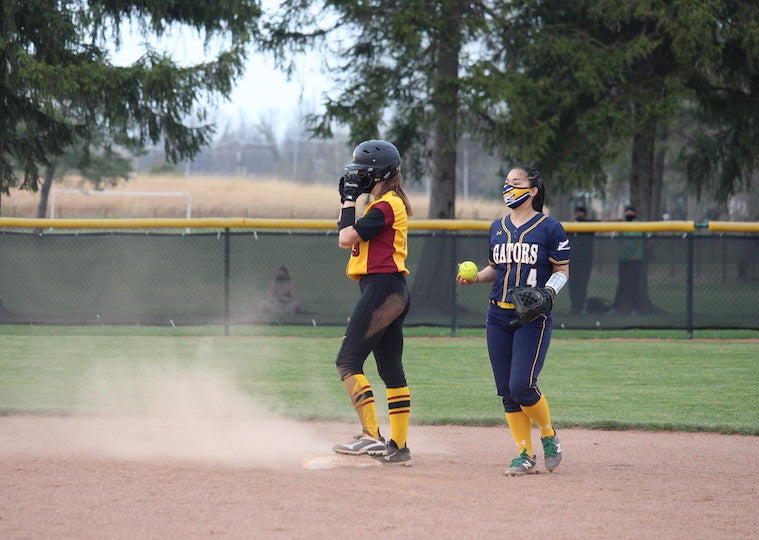 A woman softball player stands on a plate with a member of the opposing team next to her.