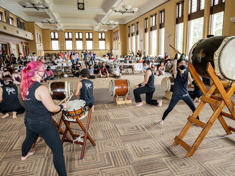 Students playing taiko drums perform in front of a large audience.