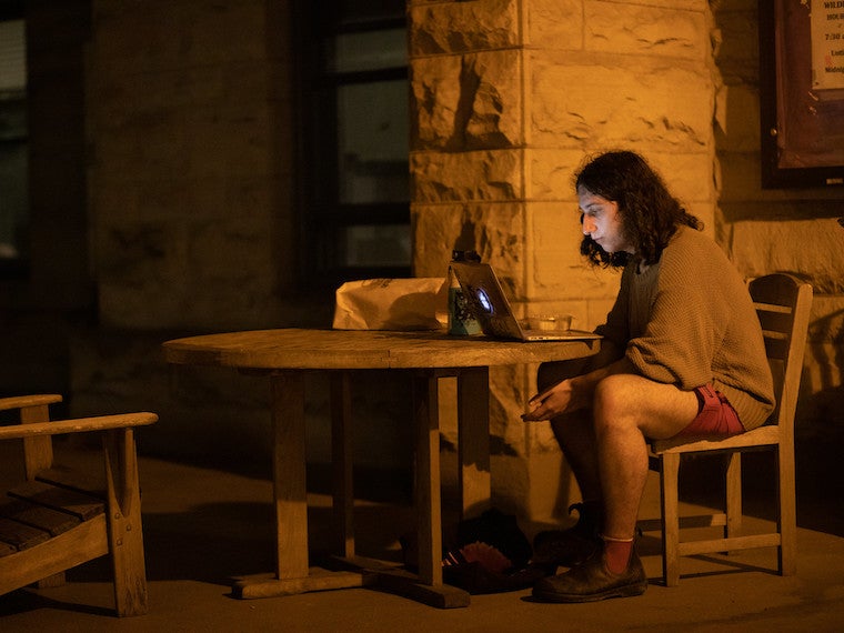 A student studies at a wooden table on a porch at night.