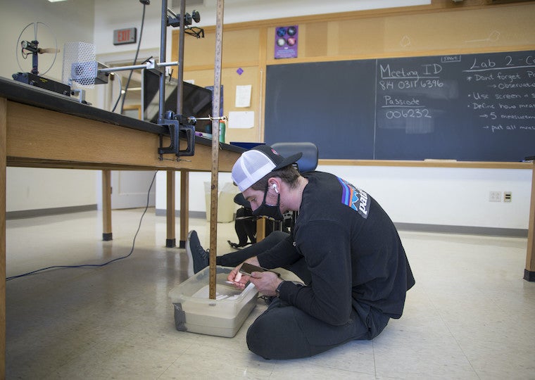 A male student uses a light on his cell phone to look into a sandbox.