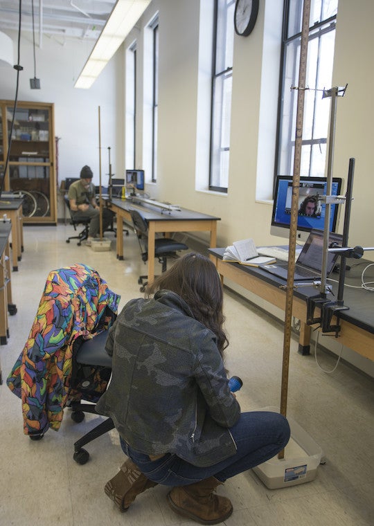 A student kneels next to a sandbox in a physics lab.