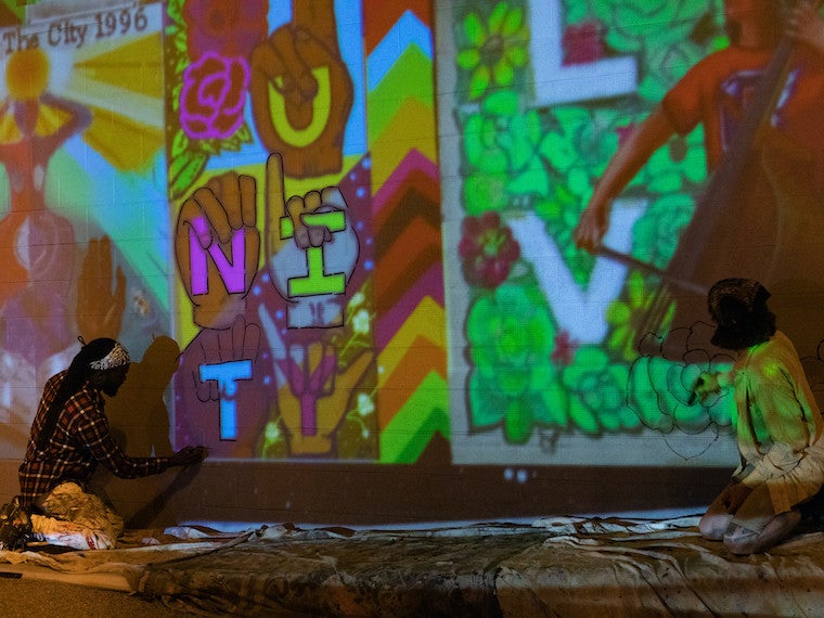 Two artists work on a mural at night.