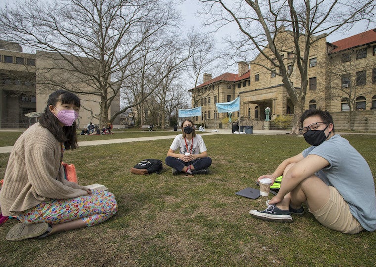 Three students eat their lunch on the lawn.