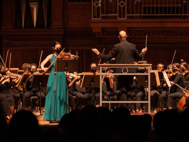 A woman plays the violin in front of an orchestra.
