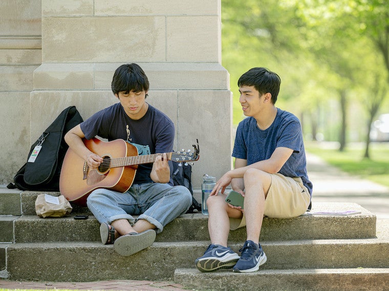 A student plays guitar outside.