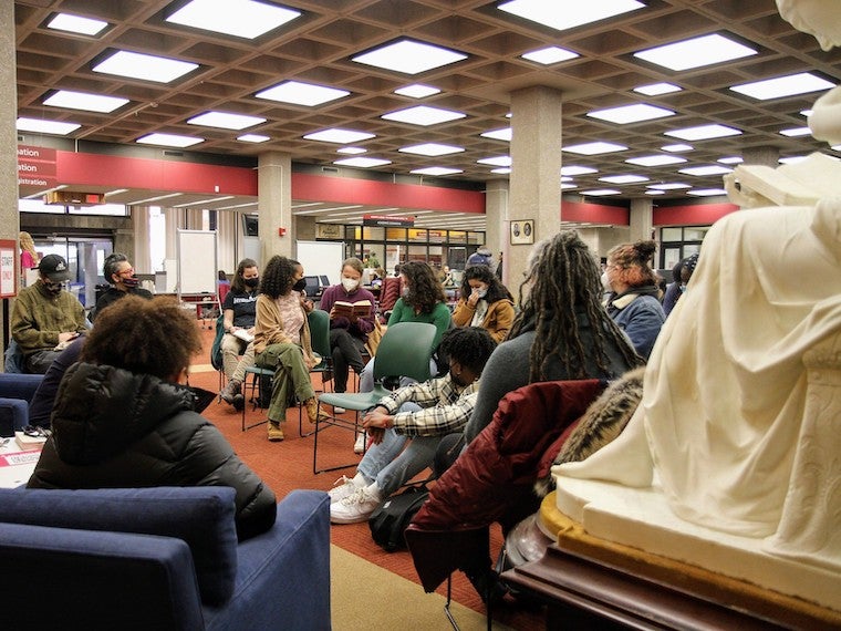 A group of people listen to a student read a book in a library